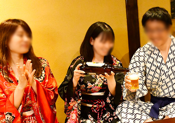 赤と黒の浴衣を着た女性二人にお酒を注がれる男性